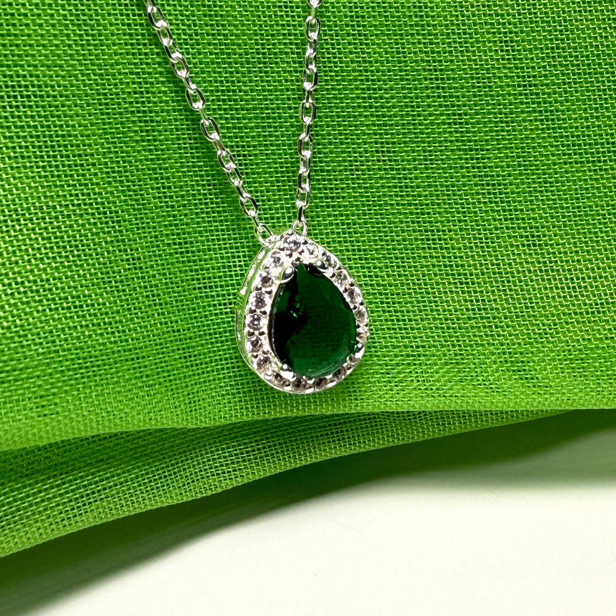 Necklace with a green teardrop pendant on a green fabric background