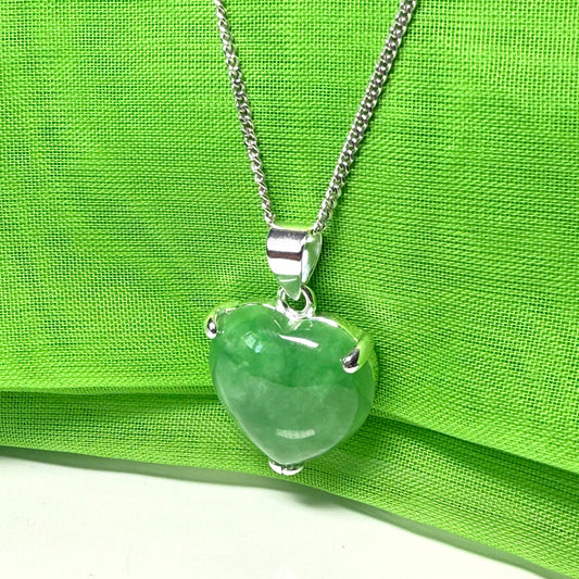 Green jade pendant on a silver chain against a green fabric background