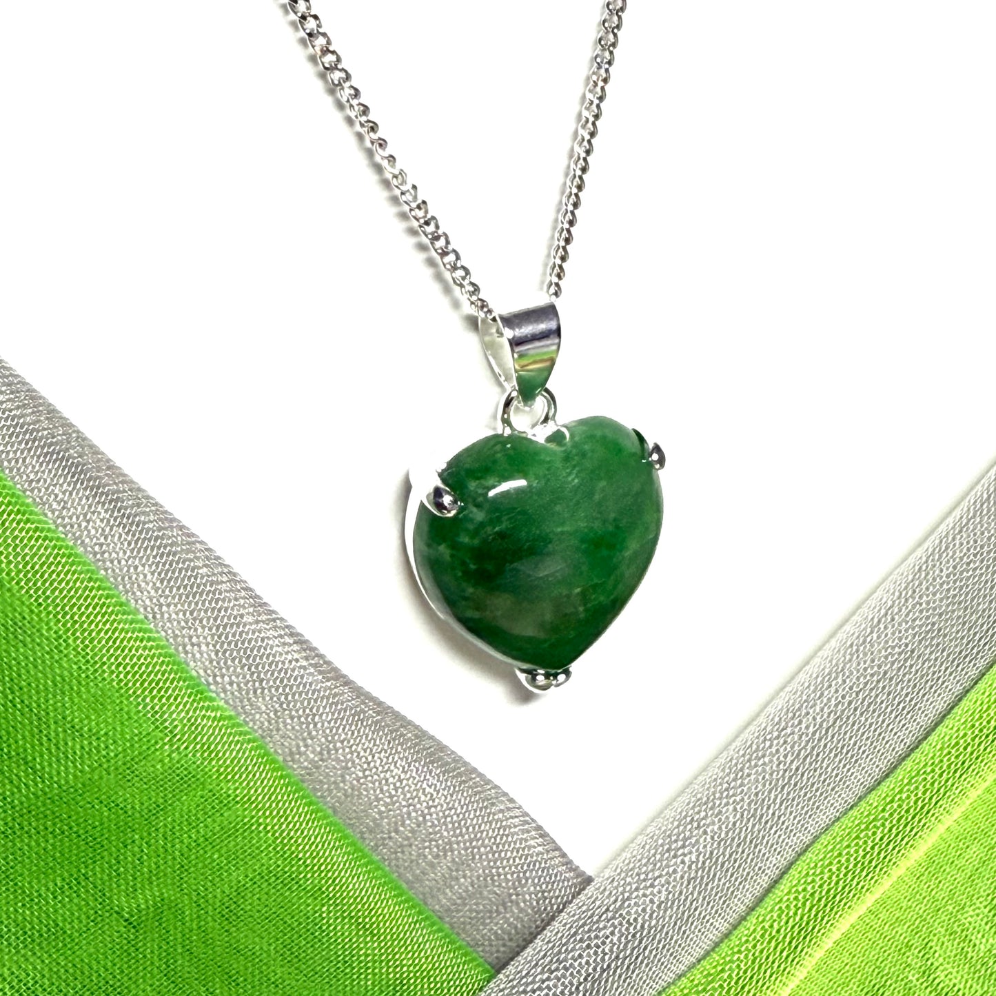 Green heart-shaped pendant on a silver chain against a green and white fabric background