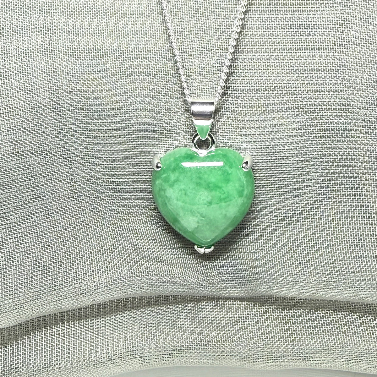 Heart-shaped green pendant on a silver chain against a gray fabric background