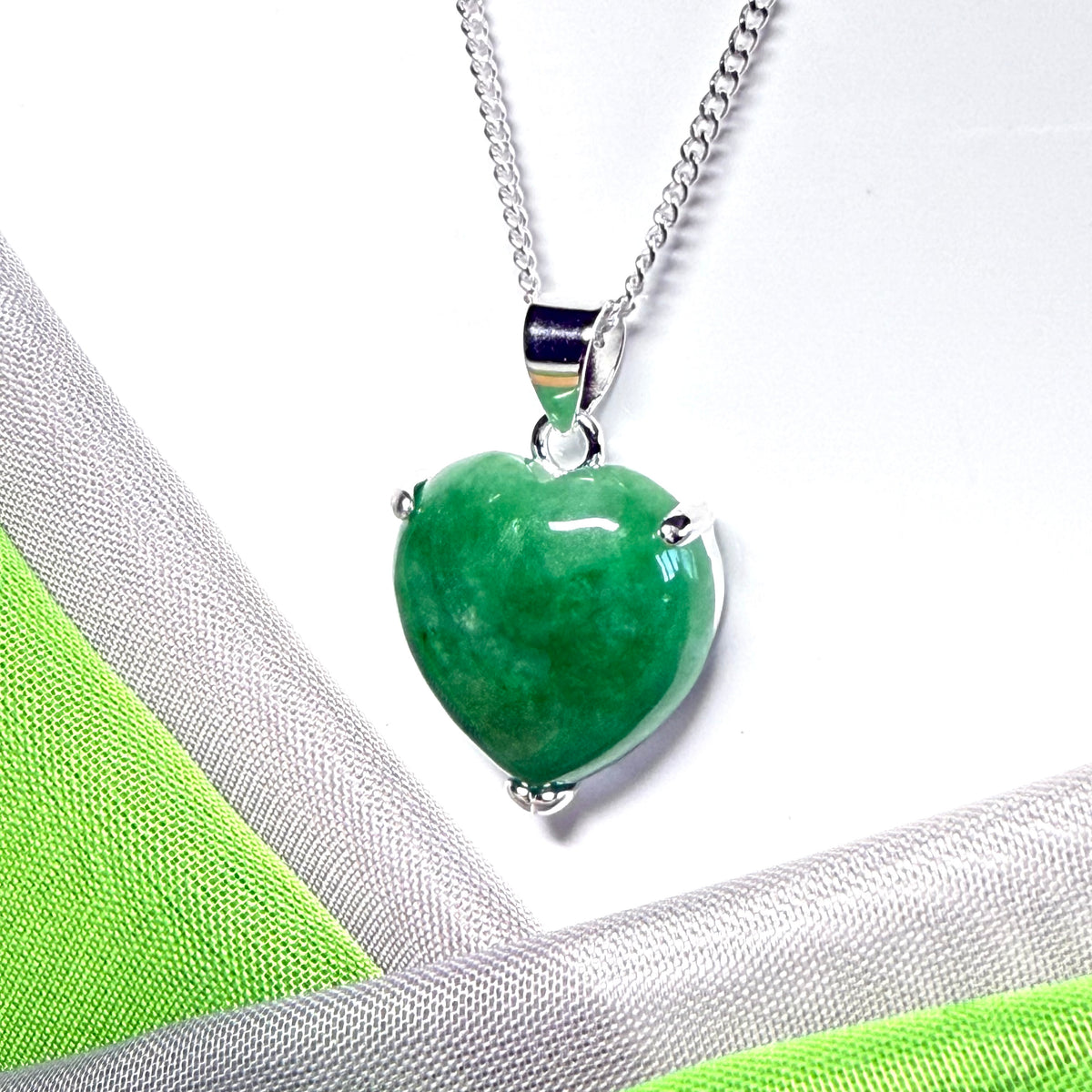 Green heart-shaped pendant on a silver chain against a white and green fabric background