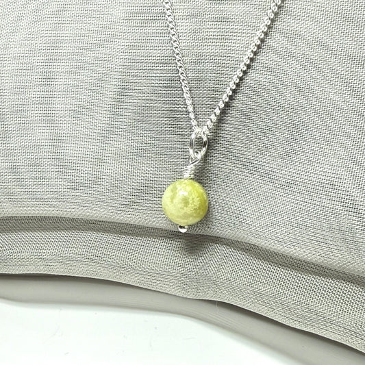 Necklace with a green bead pendant on a gray fabric background