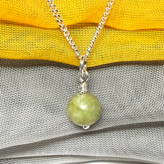Necklace with a green bead pendant on a yellow and gray fabric background