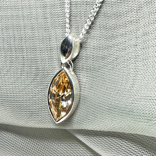 Silver pendant with a teardrop-shaped gemstone on a light gray fabric background