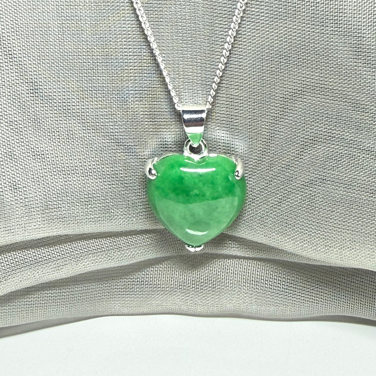 Green heart-shaped pendant on a silver chain against a gray fabric background