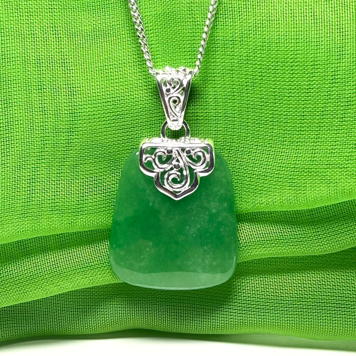 Green sea glass pendant with silver decorative clasp on a green fabric background