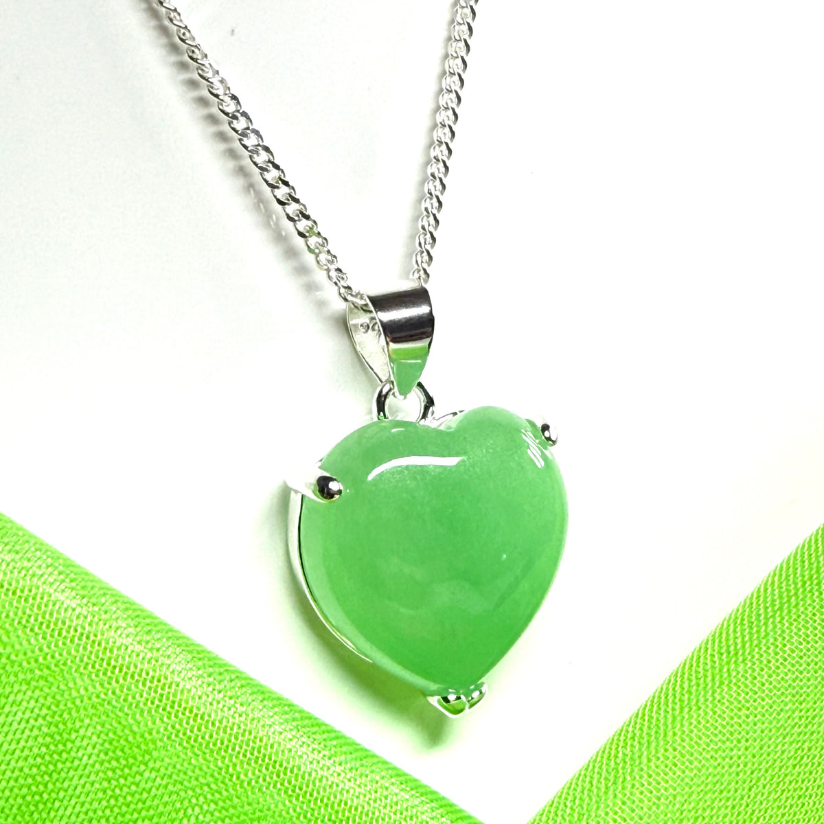 Green heart-shaped pendant on a silver chain against a green fabric background
