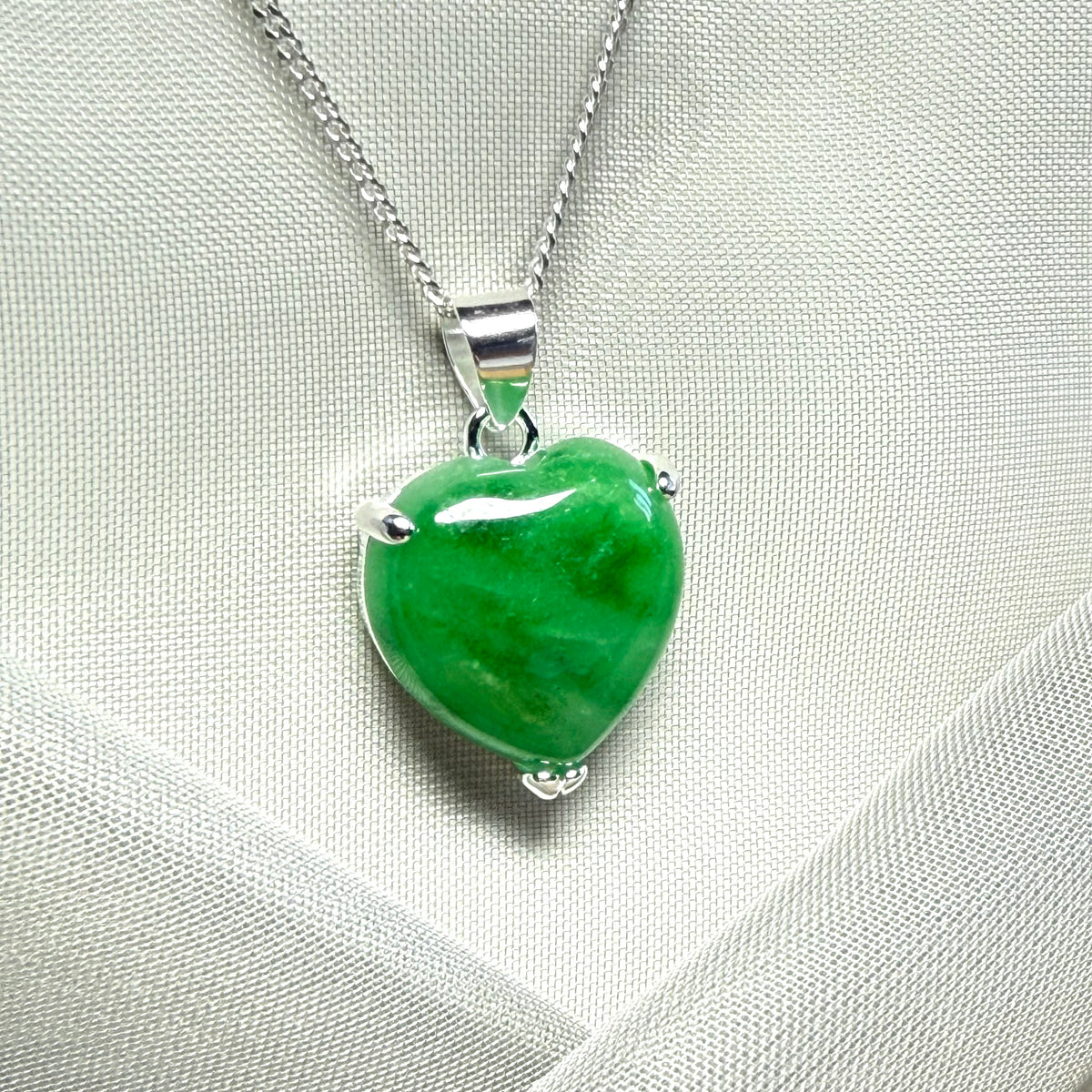 Green heart-shaped pendant on a silver chain against a light gray background