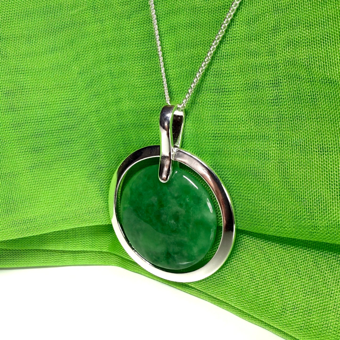 Green jade pendant with silver circle on a green fabric background