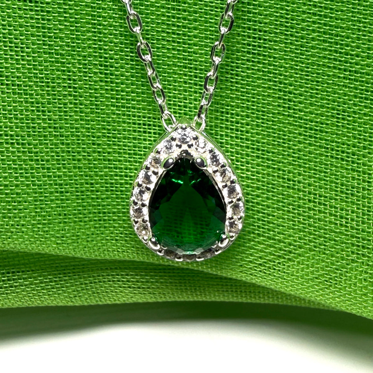 Green teardrop pendant necklace on a green fabric background