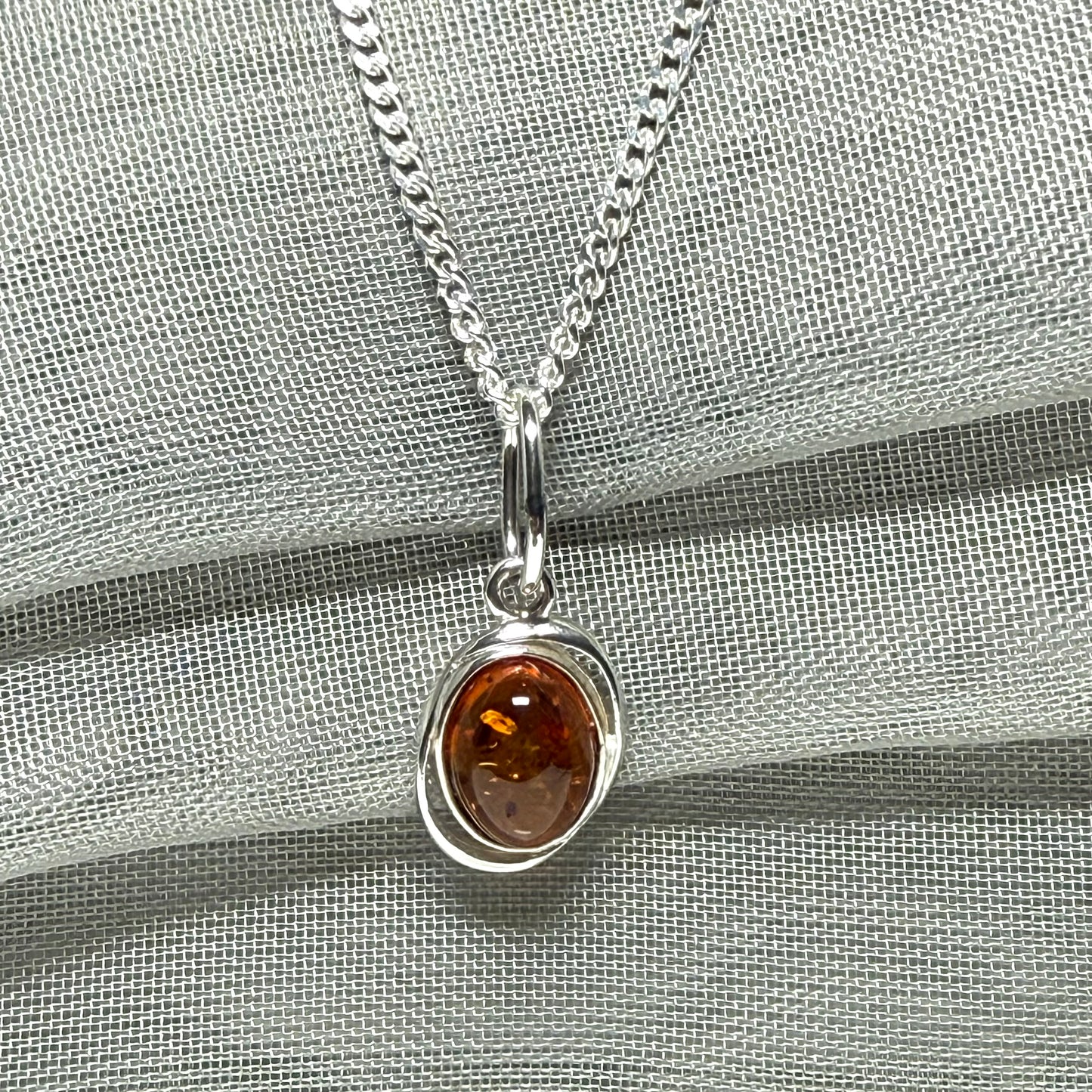 Orange real amber oval sterling silver necklace with a swirl set open pierced pendant