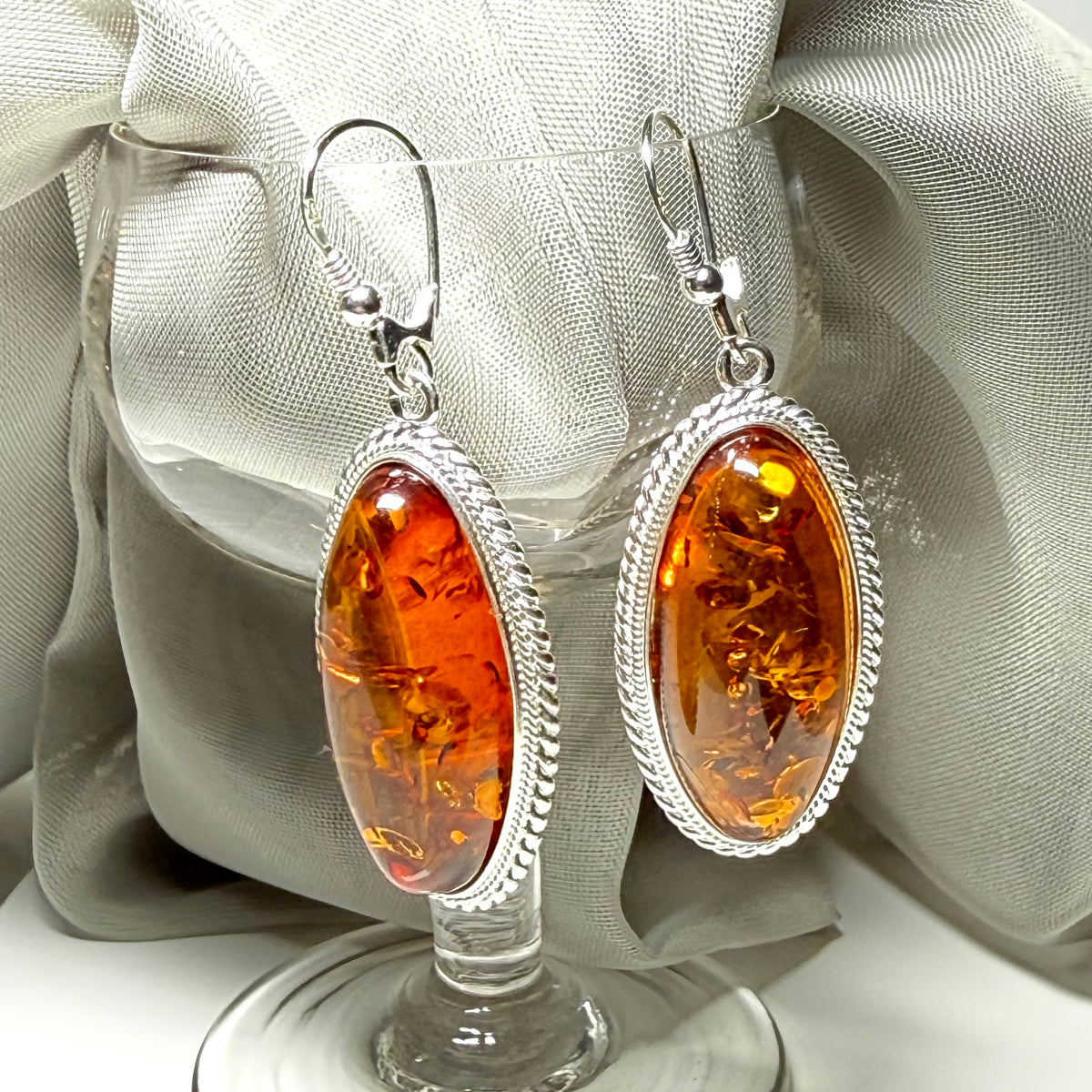 A pair of real amber drop earrings an oval shape rope edged sterling silver continental wired fittings