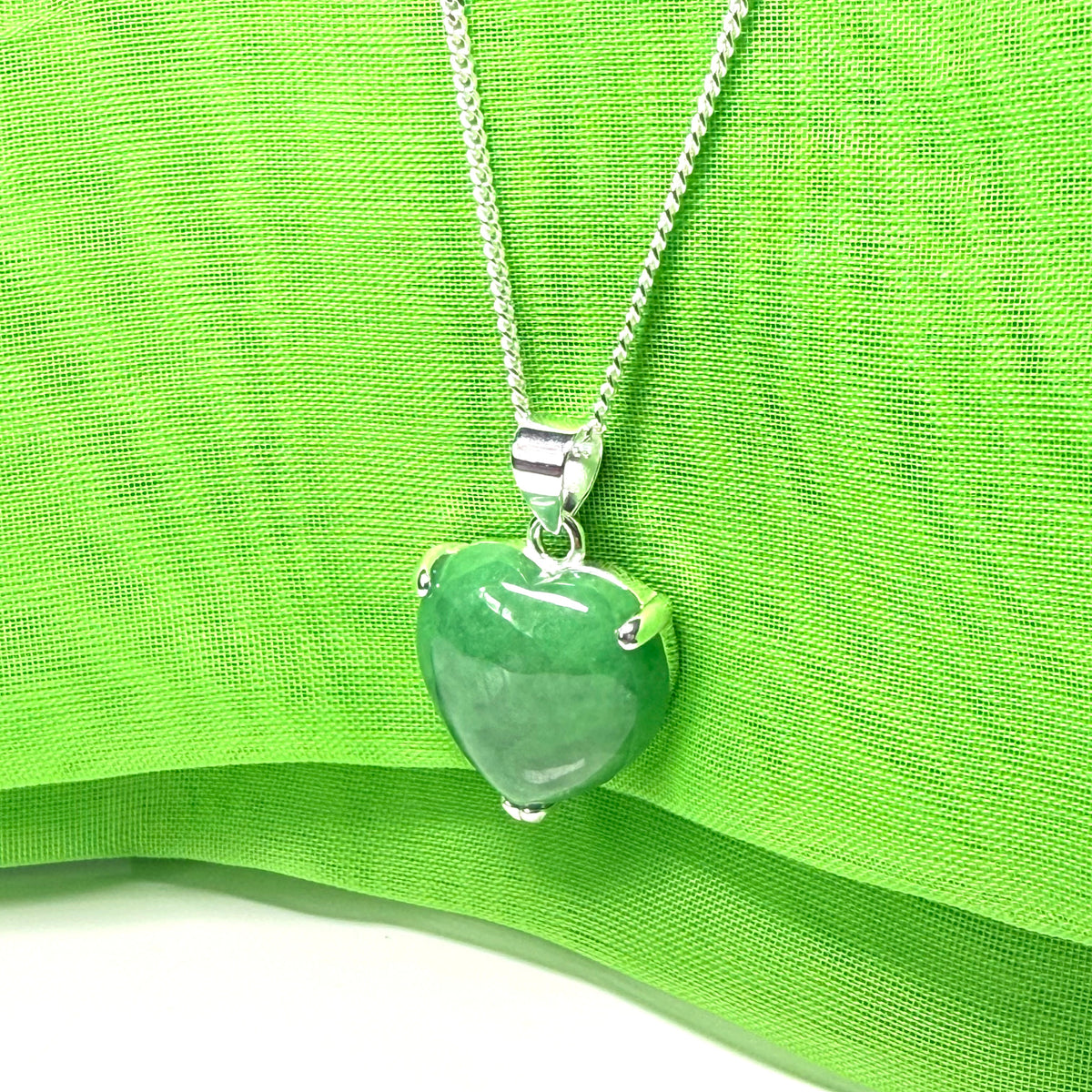 Green heart-shaped pendant on a silver chain against a green fabric background