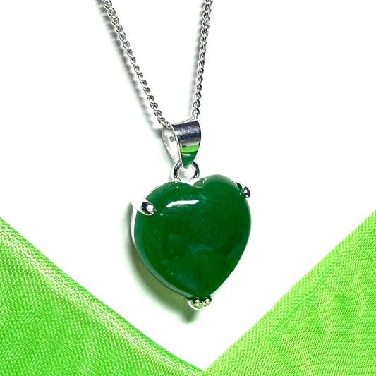Real green jade heart-shaped pendant on a silver chain against a green fabric background