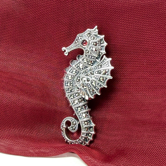 Silver seahorse brooch with real red garnet gemstone and real marcasite stones on a red fabric background