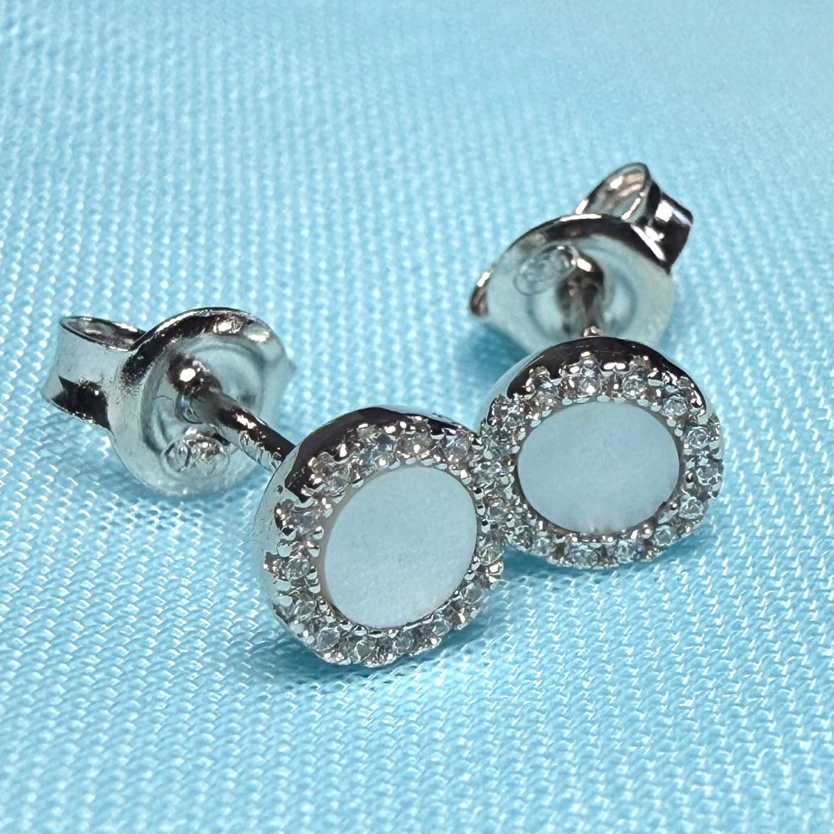 Silver stud earrings with clear gemstones on a light blue fabric background