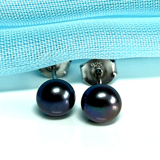 Pair of black pearl earrings on a light blue fabric background
