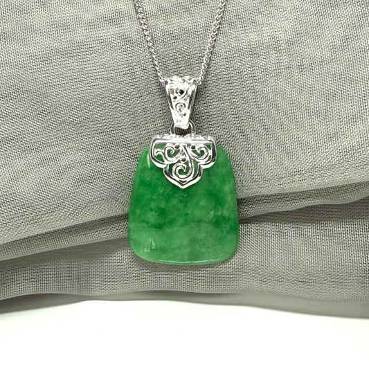 Real dark green jade pendant with silver chain on a gray fabric background