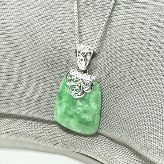 Green pendant necklace with silver chain on a gray fabric background