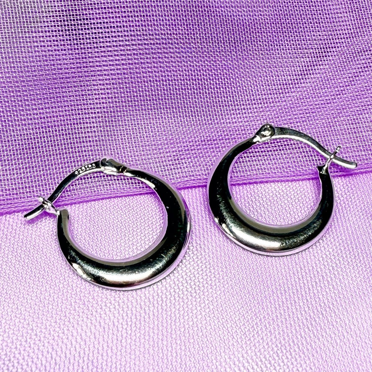 Silver hoop earrings on a purple fabric background