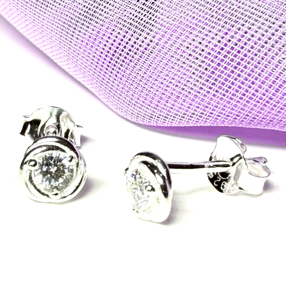 Silver stud earrings with clear gemstones on a light purple fabric background