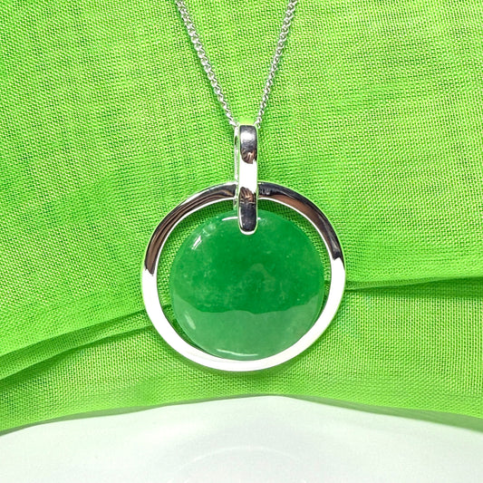 Necklace with a real green jade pendant and silver ring on a green fabric background
