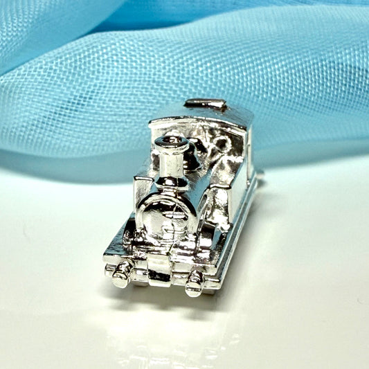 Small silver toy train charm on a light blue fabric background