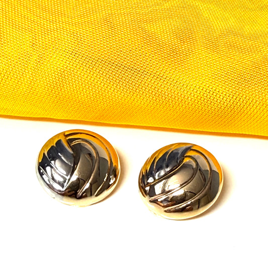 Gold and white gold circular earrings on a yellow fabric background