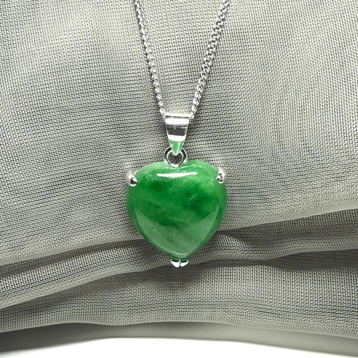 Green heart-shaped pendant on a silver chain against a gray fabric background