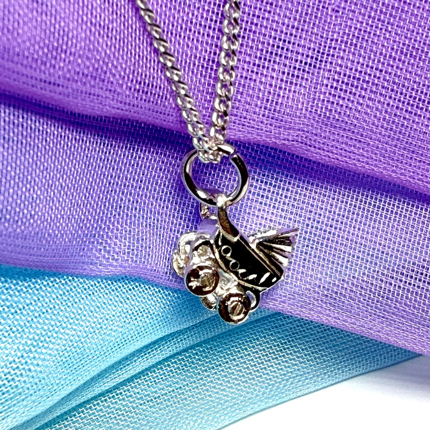 A silver-toned metal snowmobile pendant necklace on a matching chain, displayed against a draped purple and light blue mesh fabric background.