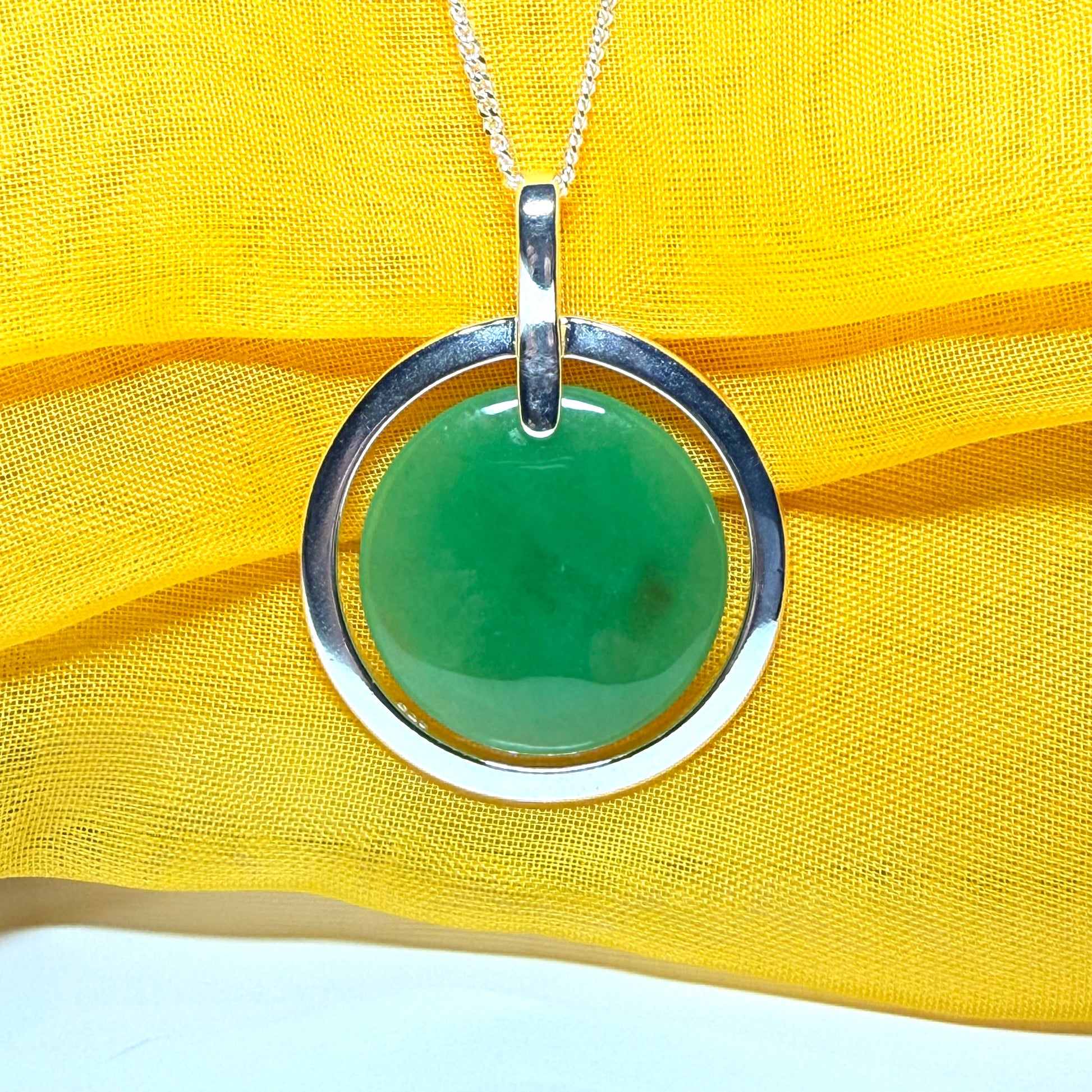 Green pendant with silver ring on yellow fabric