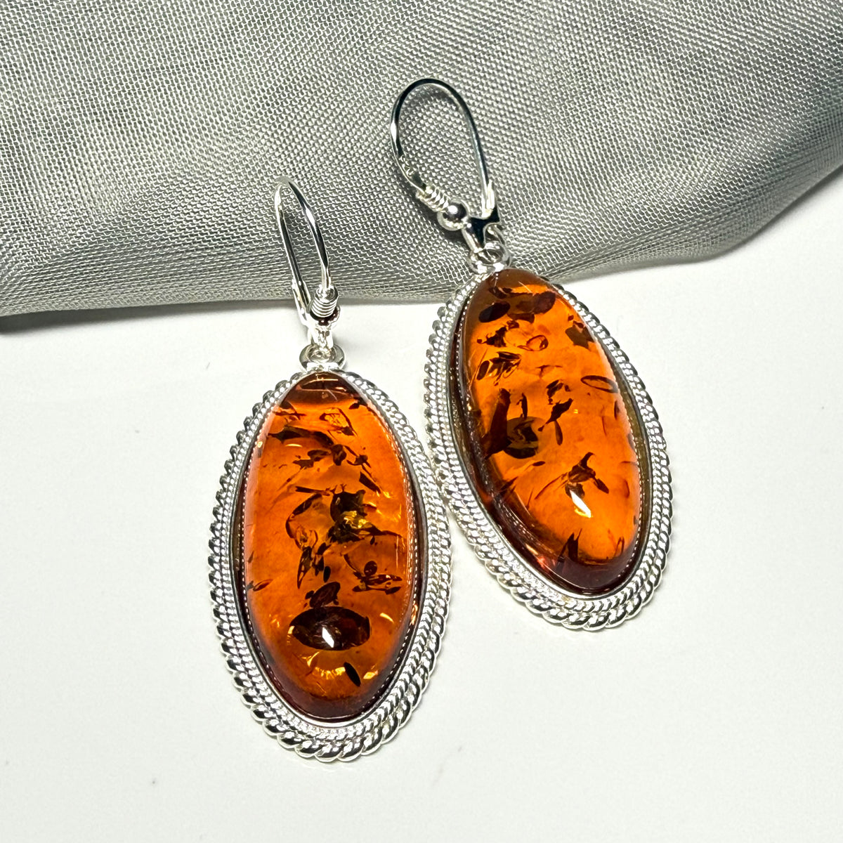 A pair of real amber drop earrings an oval shape rope edged sterling silver continental wired fittings