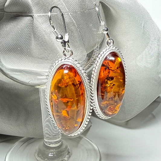 A pair of real amber drop earrings an oval shape rope edged sterling silver continental wired fittings