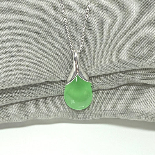 Necklace with a real green jade teardrop pendant on a silver chain against a gray fabric background