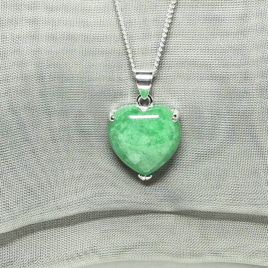 Heart-shaped green pendant on a silver chain against a gray fabric background