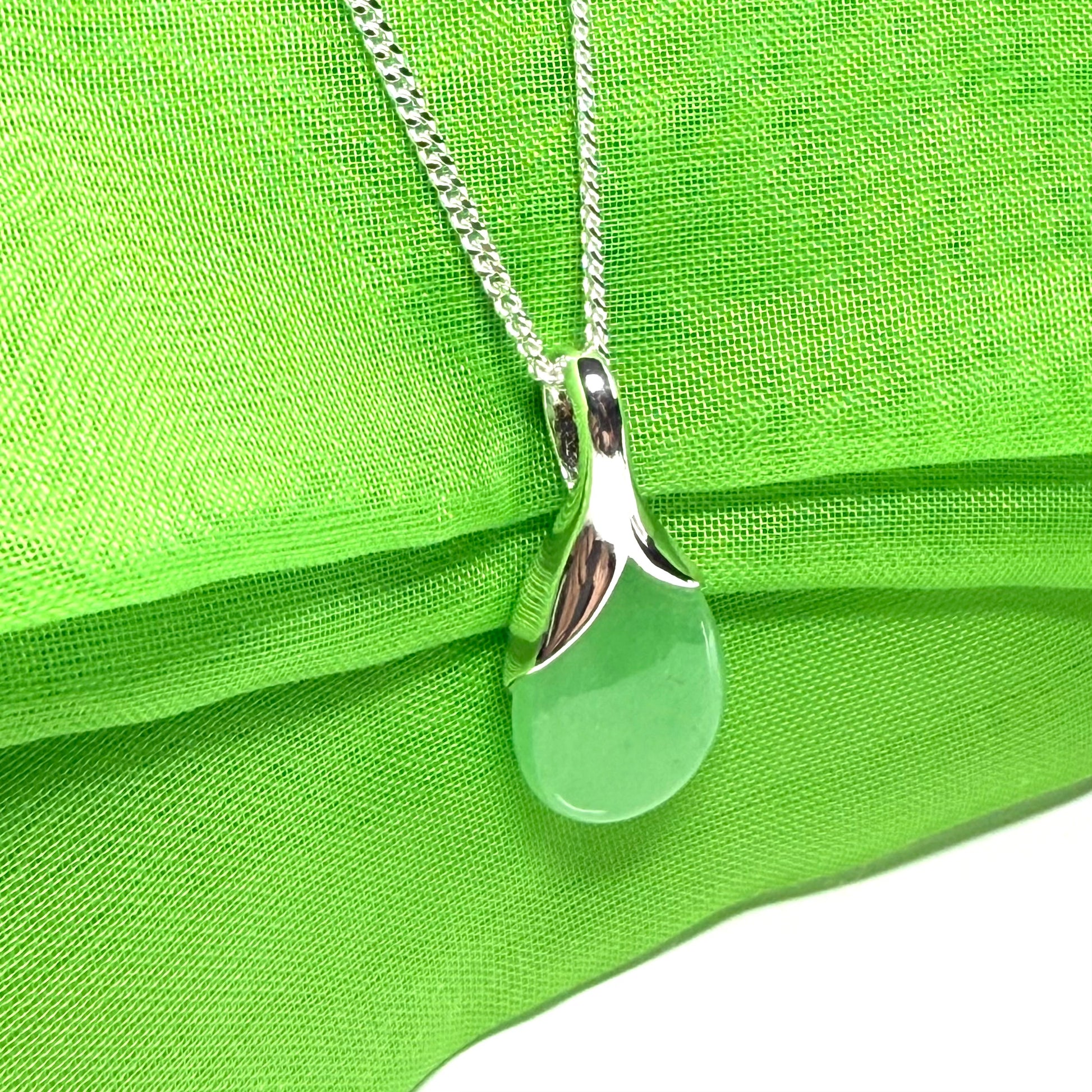 Green teardrop pendant on a silver chain against a green fabric background