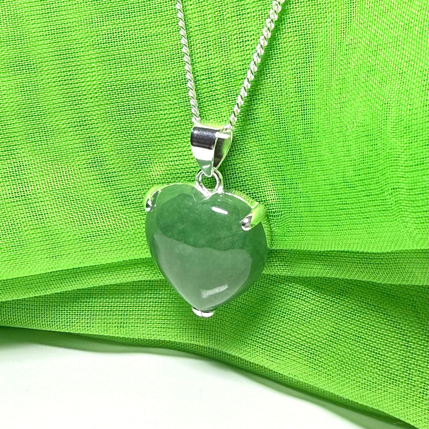 Heart-shaped green pendant on a silver chain against a green fabric background