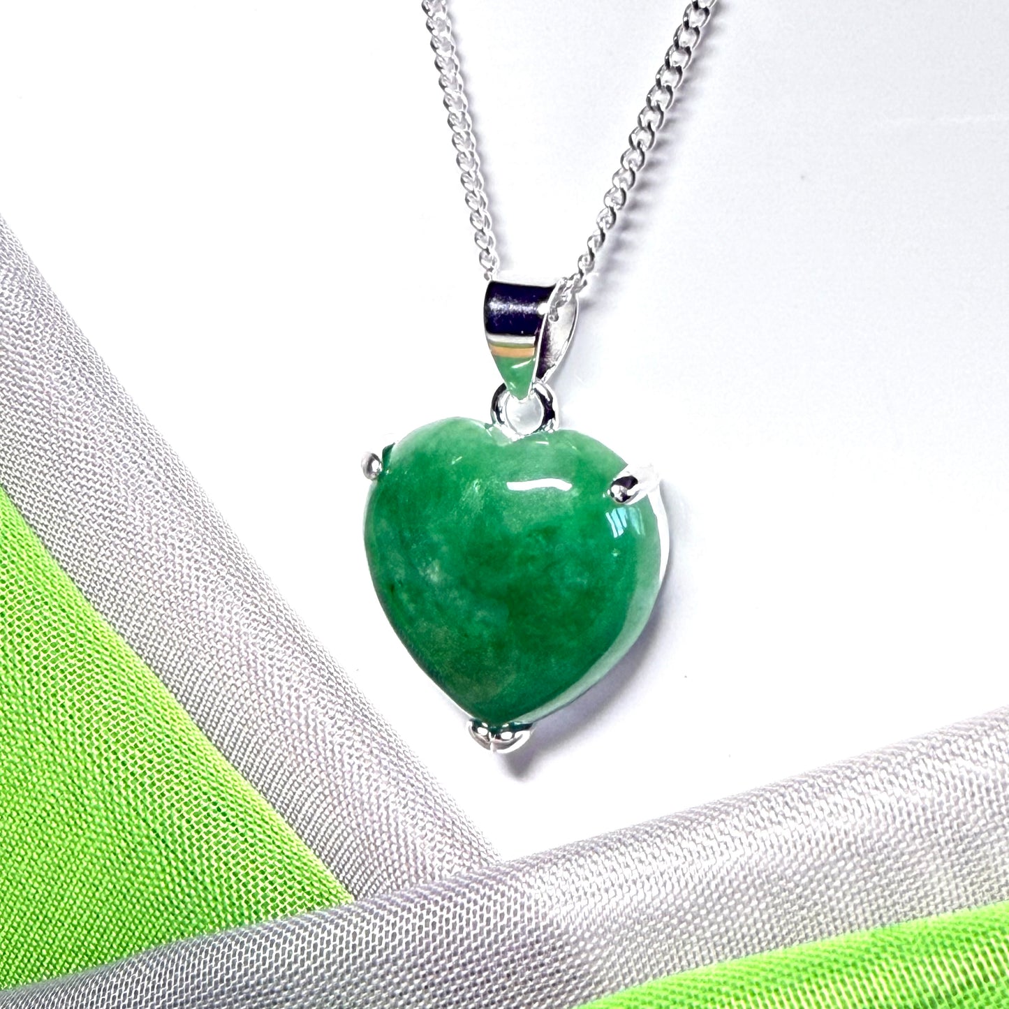 Green heart-shaped pendant on a silver chain against a white and green fabric background