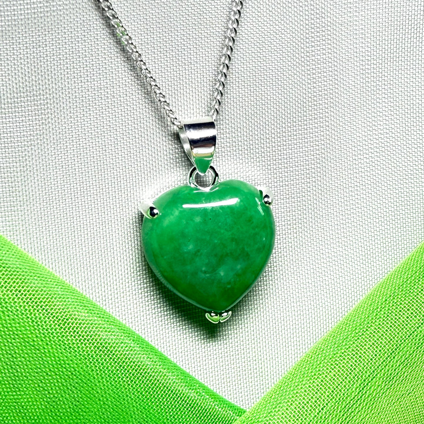 Green heart-shaped pendant on a silver chain against a green fabric background
