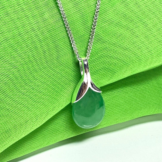 Green teardrop pendant on a silver chain against a green fabric background