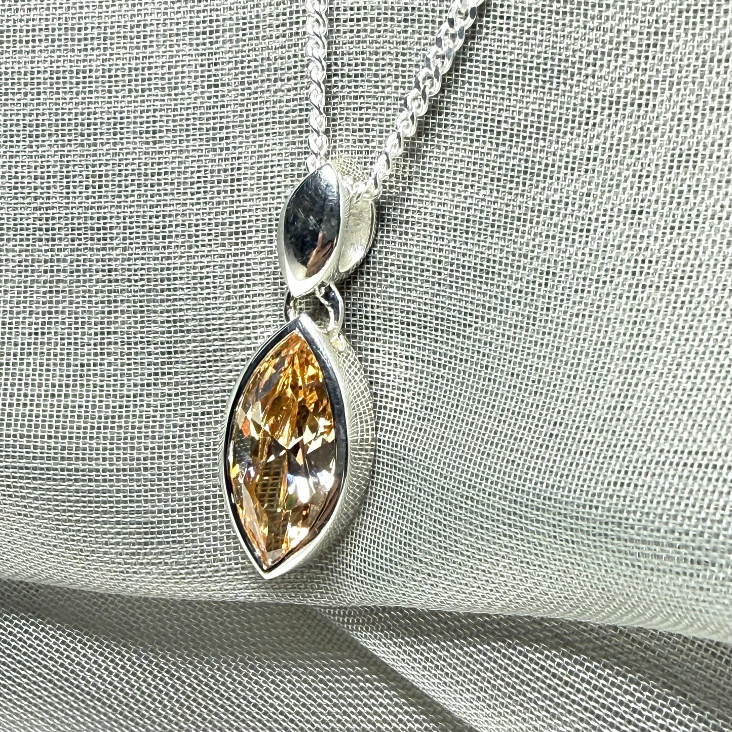 Silver pendant with a teardrop-shaped gemstone on a light gray fabric background