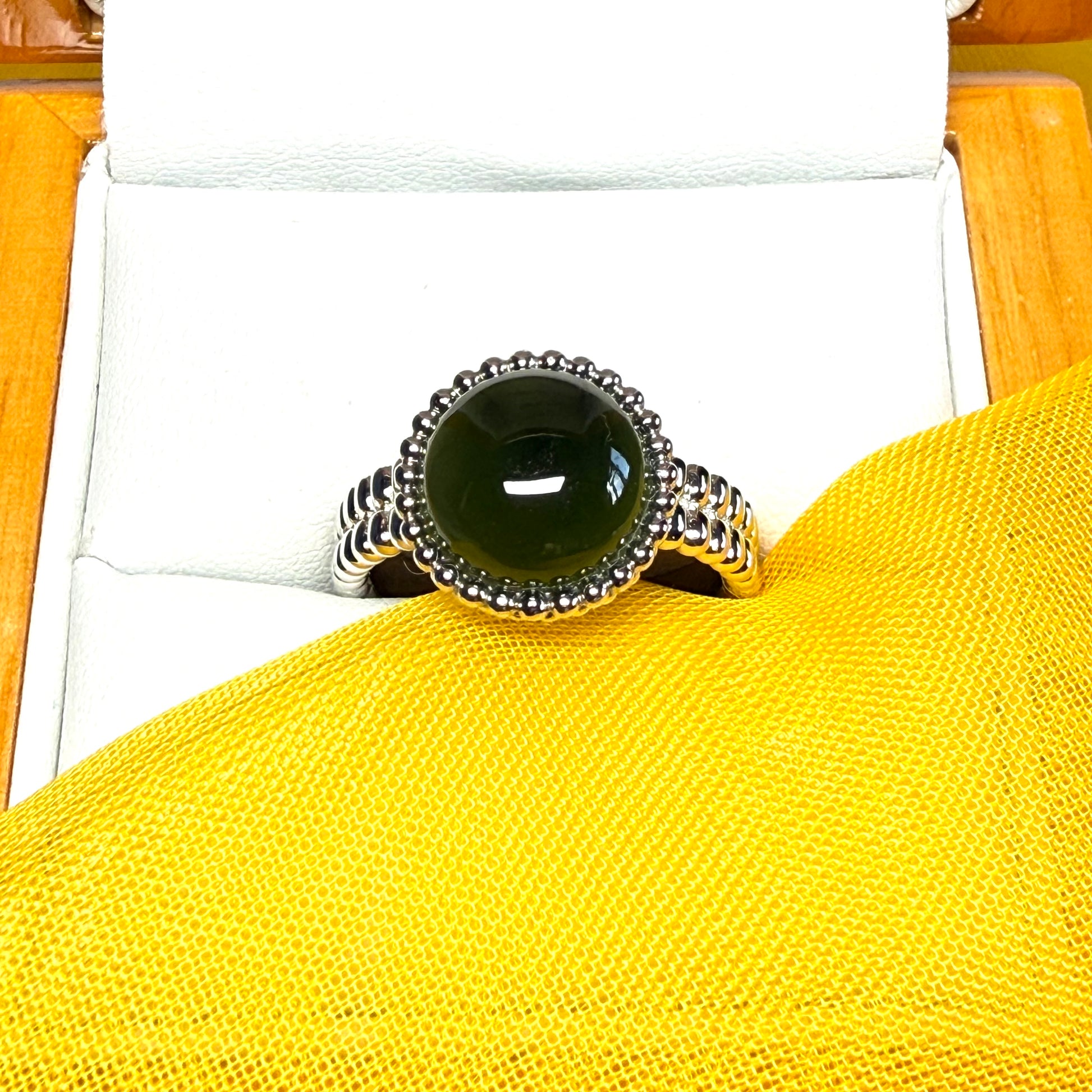 Silver ring with a black gemstone on a yellow surface
