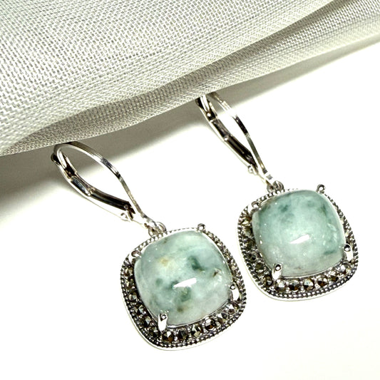Pair of earrings with green gemstones and silver frames on a white background