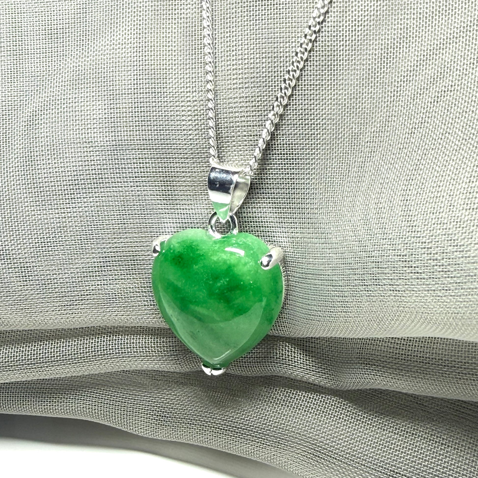 Green heart-shaped pendant on a silver chain against a gray fabric background