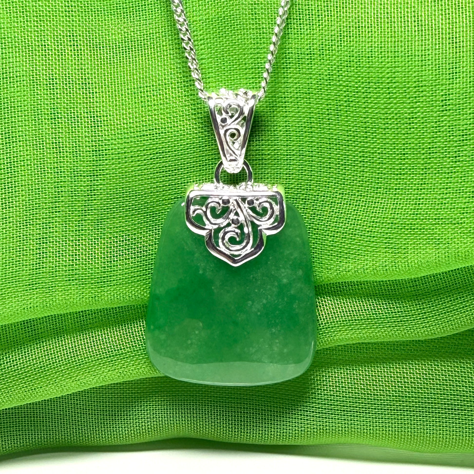 Green sea glass pendant with silver decorative clasp on a green fabric background