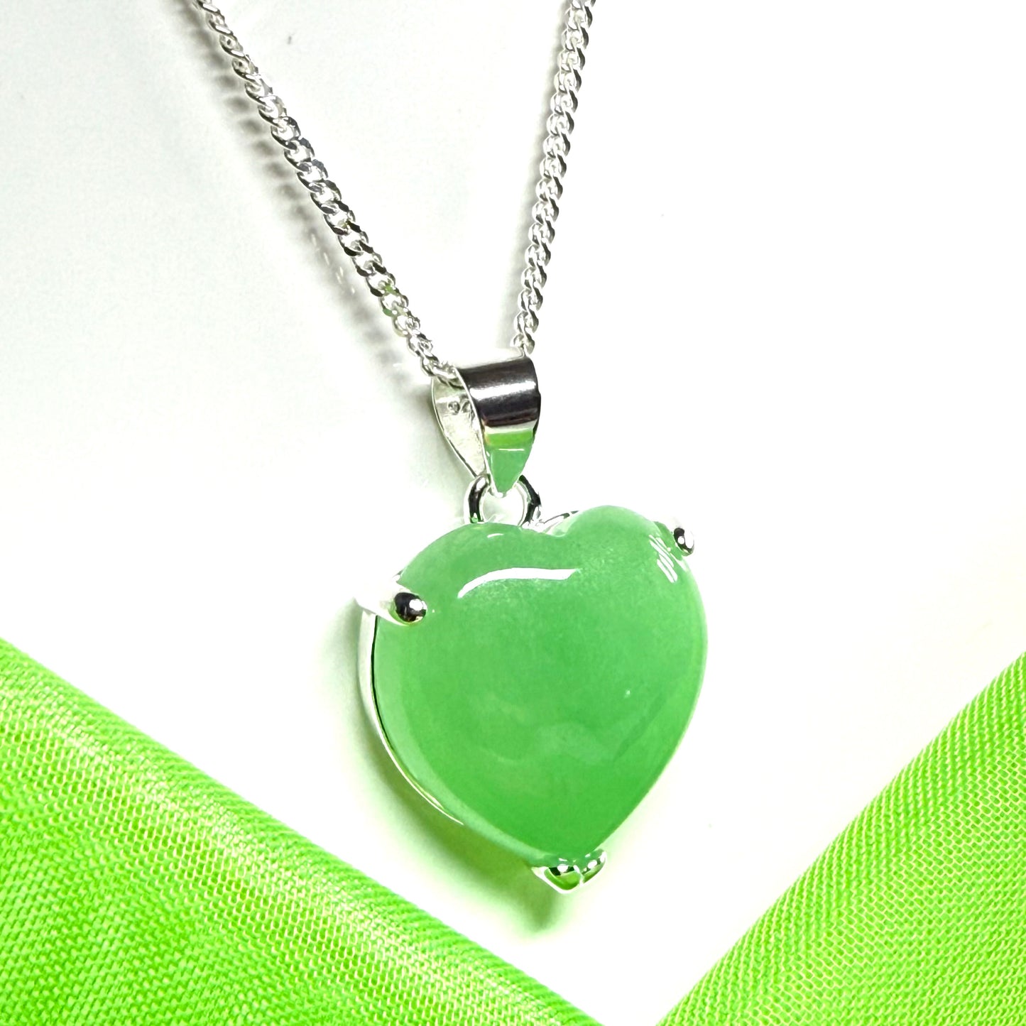 Green heart-shaped pendant on a silver chain against a green fabric background