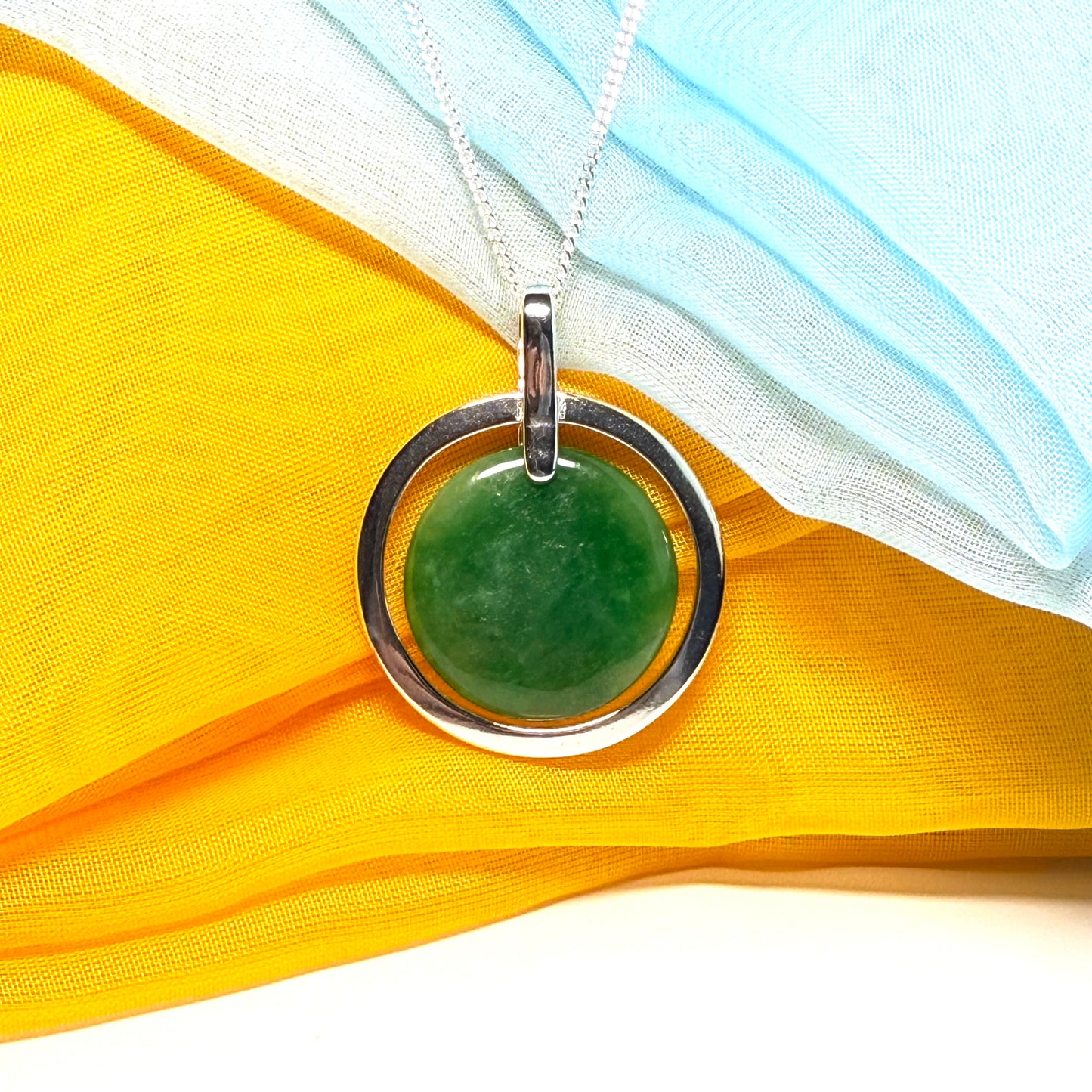 Green stone pendant in a silver circle on a yellow fabric background