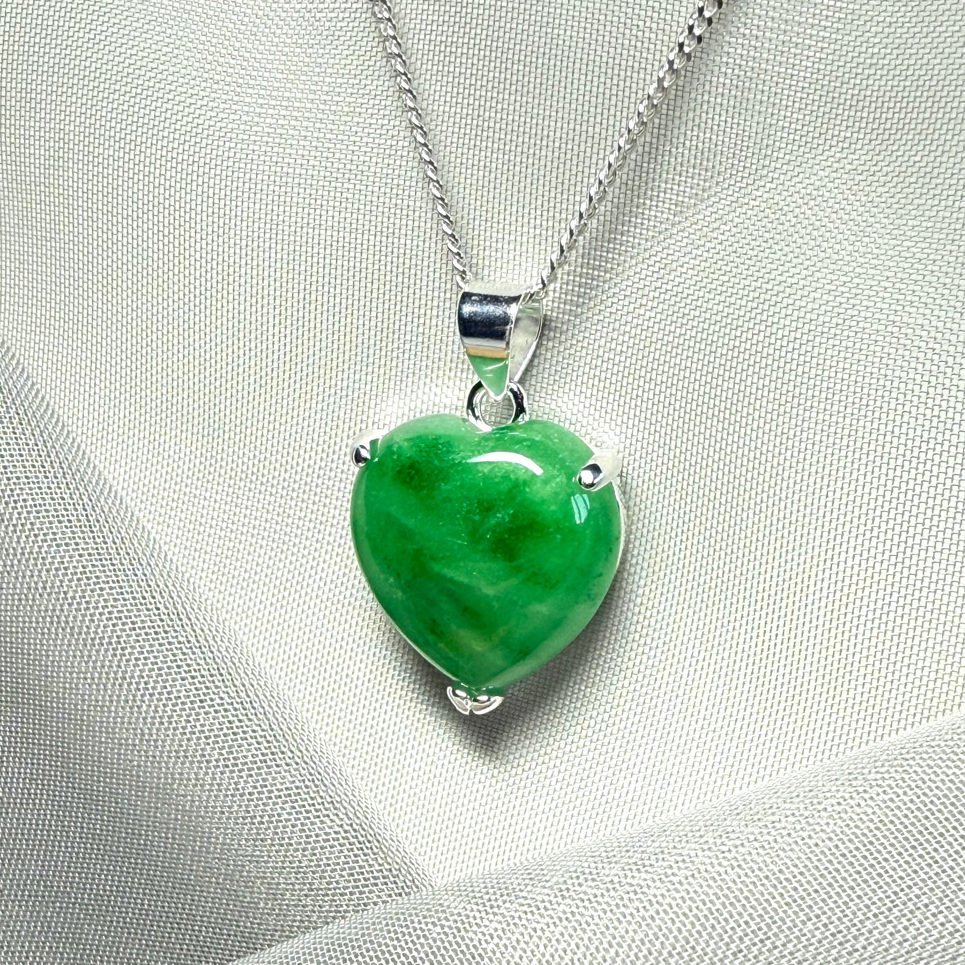Green heart-shaped pendant on a silver chain against a light gray background