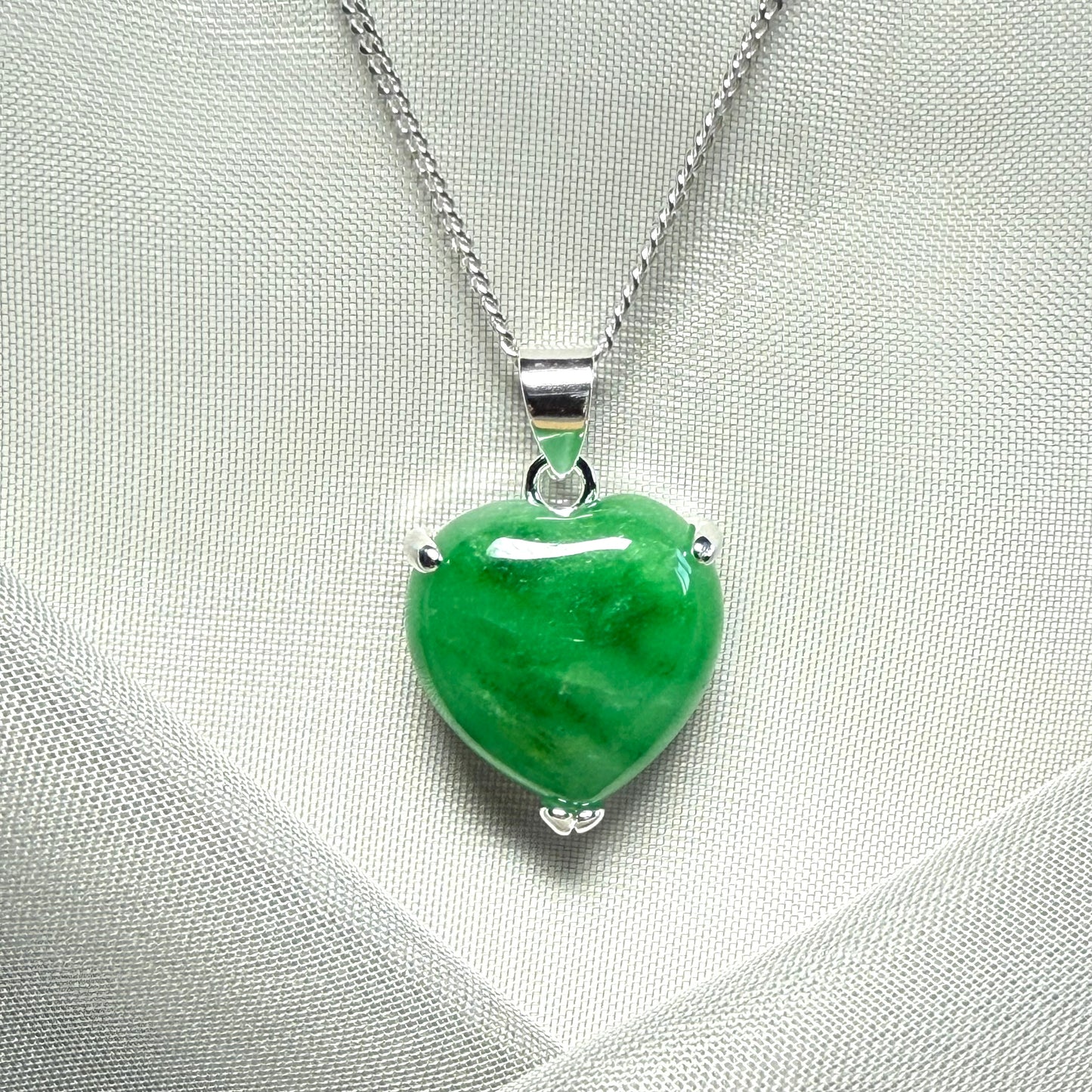 Green heart-shaped pendant on a silver chain against a light gray background