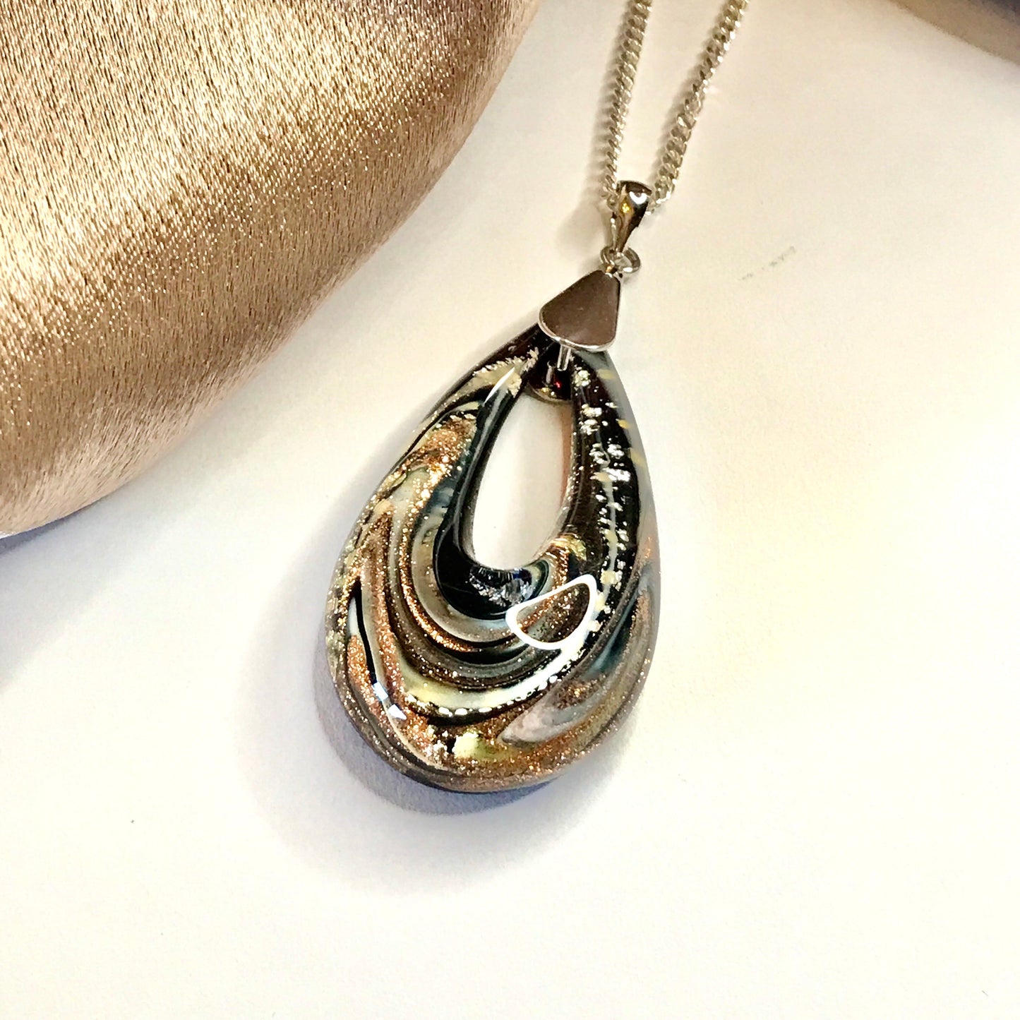 Teardrop-shaped pendant on a chain against a neutral background
